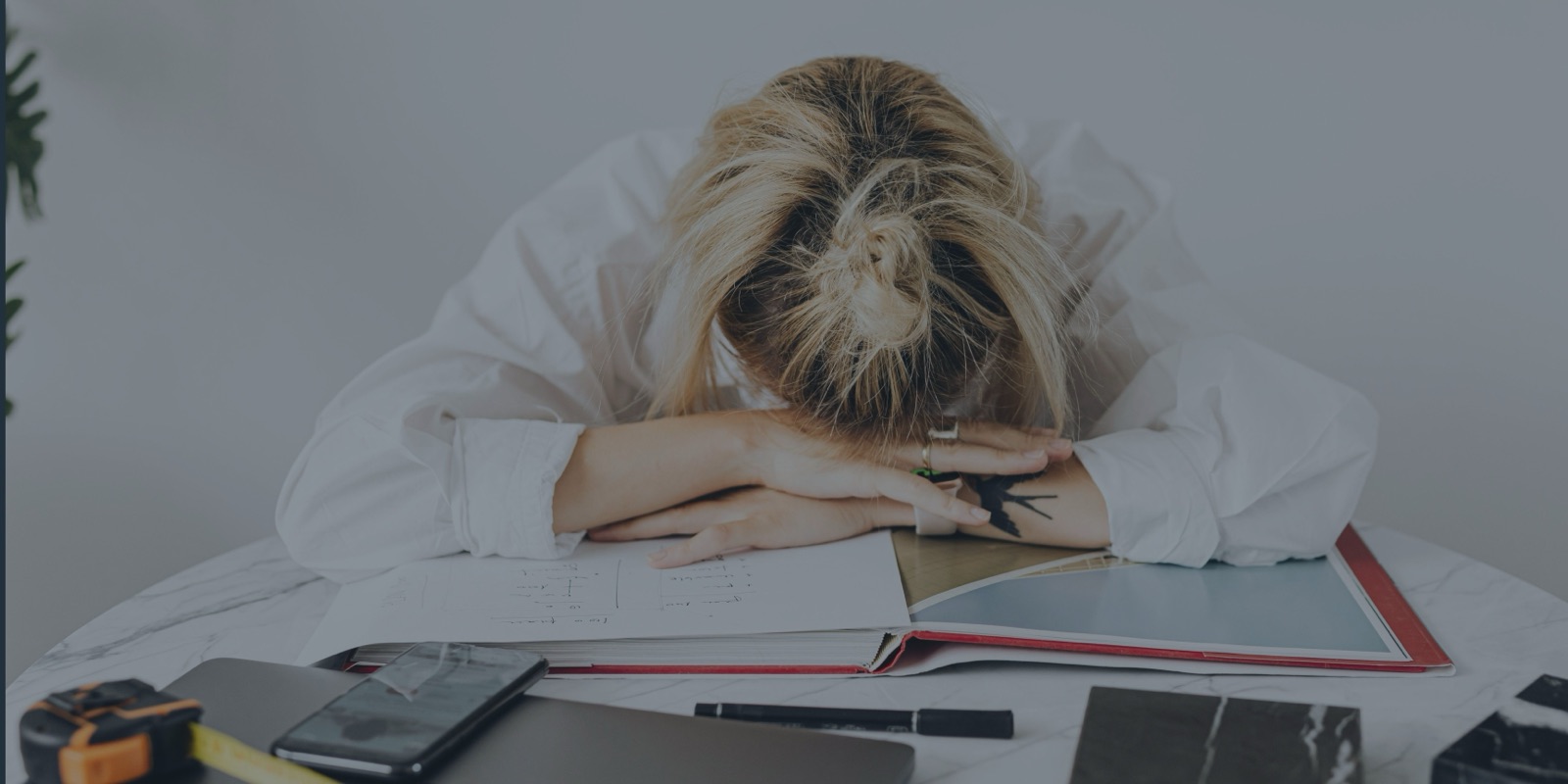 Femme épuisée, la tête posée sur son bureau au milieu de ses dossiers