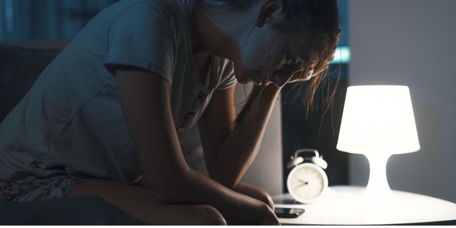 Femme épuisée assise sur son lit la nuit, la tête dans la main, près d'une lampe de chevet